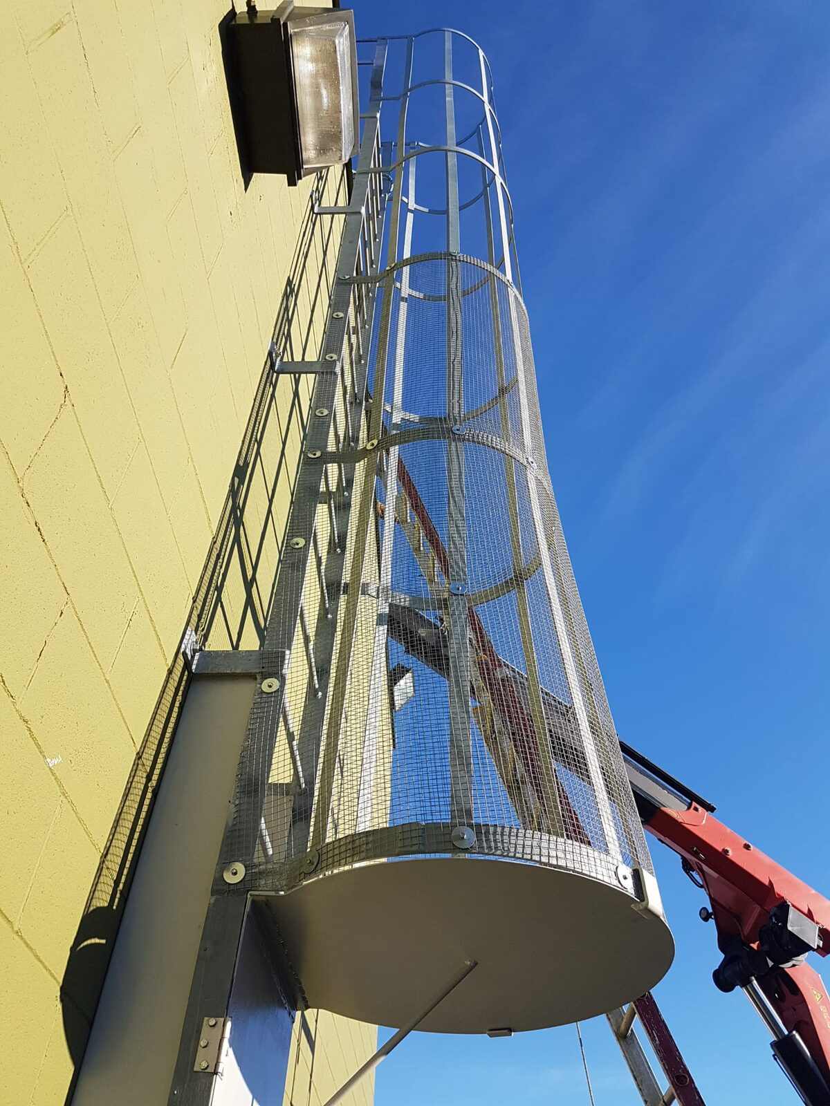 Galvanized fixed vertical access ladder with a mesh safety cage mounted on an industrial building wall
