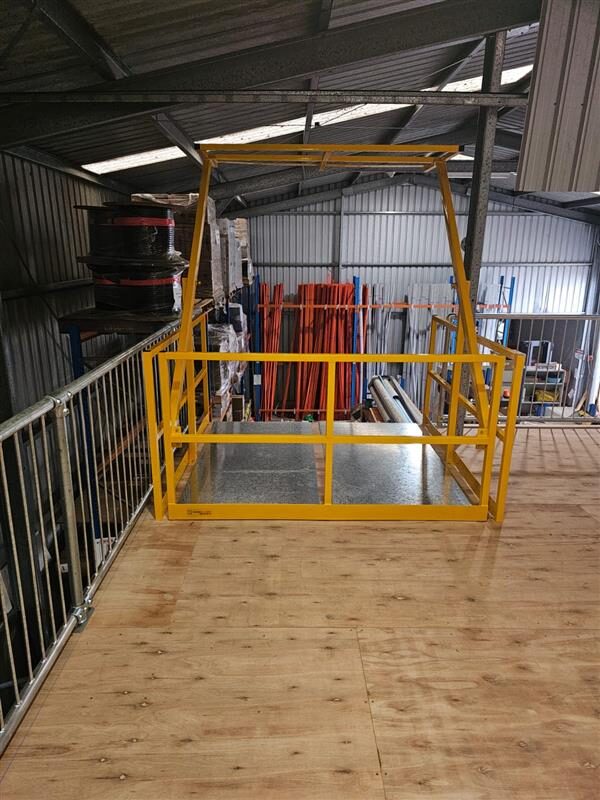 Yellow self-closing steel safety gate guarding the open edge of an industrial mezzanine storage platform