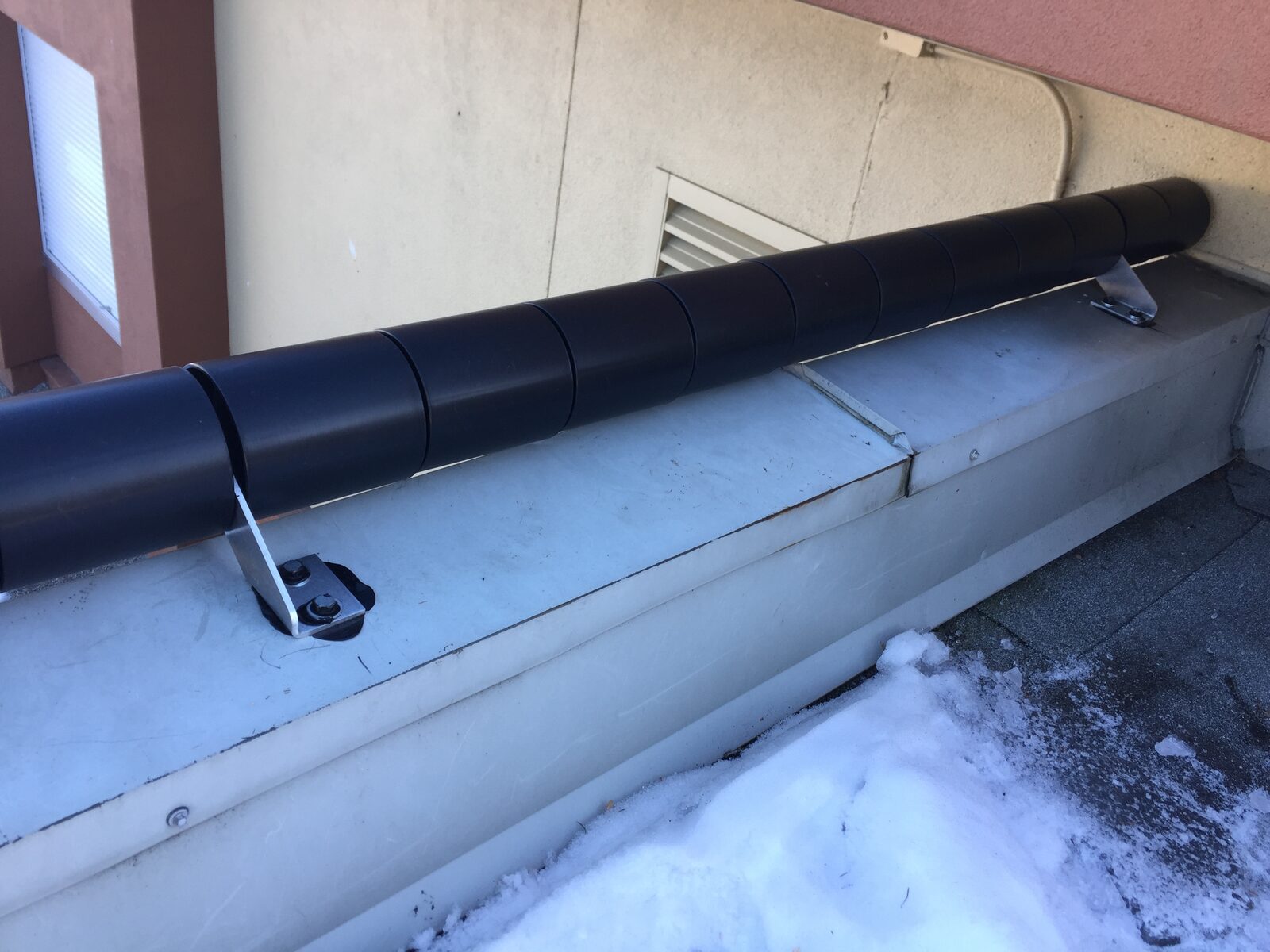 Free-spinning anti-climb roller barriers mounted along a rooftop parapet to deter unauthorized access